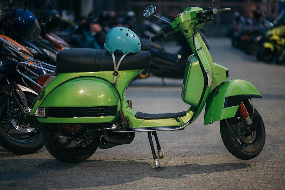 A retro green scooter with a helmet, parked among other motorbikes on an urban street.