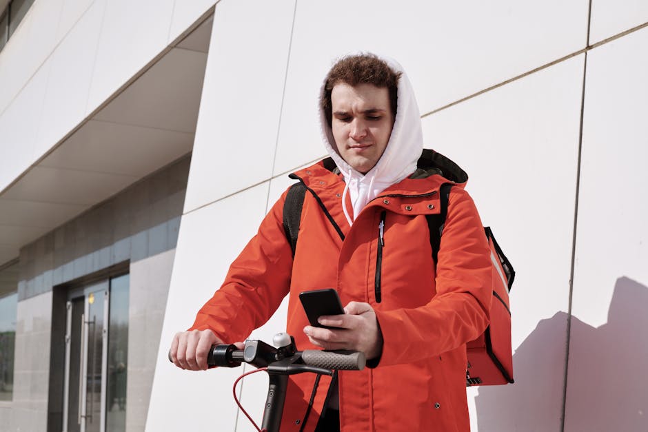 Delivery person on e-scooter using smartphone outside a modern building.