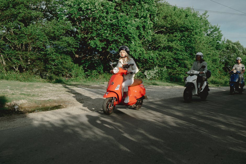 Three adults ride scooters on a sunny day, surrounded by lush greenery, enjoying the outdoors.